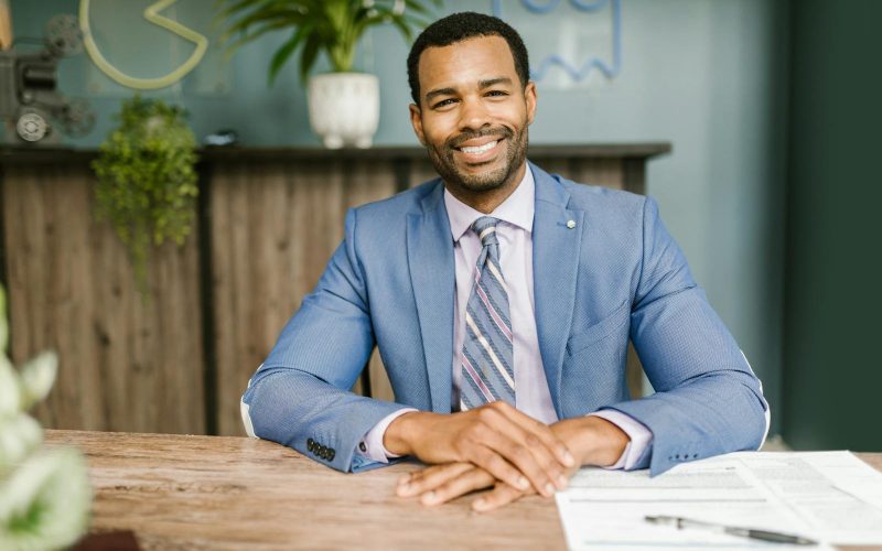 Smiling businessman in office attire sitting at a desk with documents.