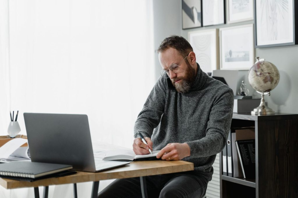 Man concentrating on work at home office desk with laptop and documents.