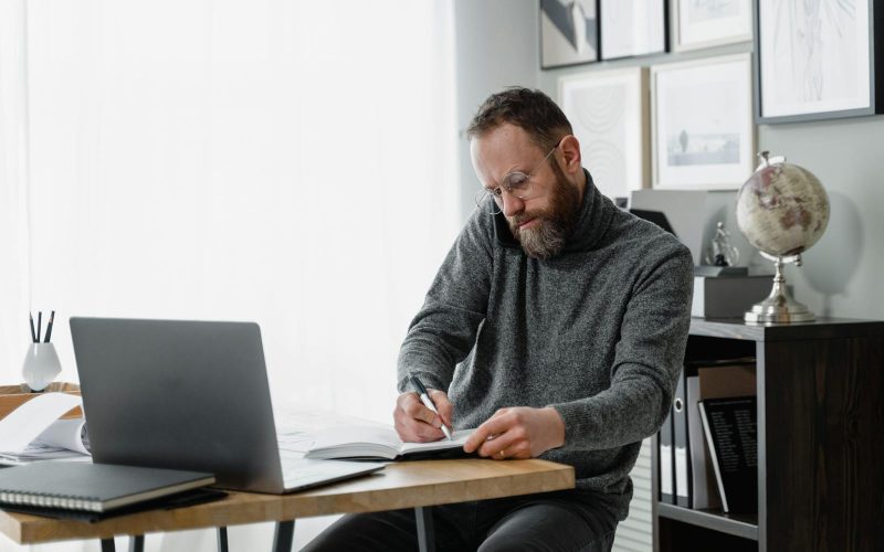 Man concentrating on work at home office desk with laptop and documents.