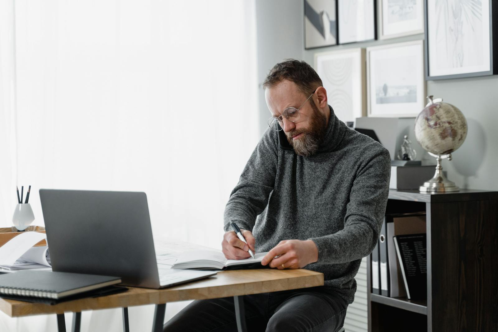 Man concentrating on work at home office desk with laptop and documents.