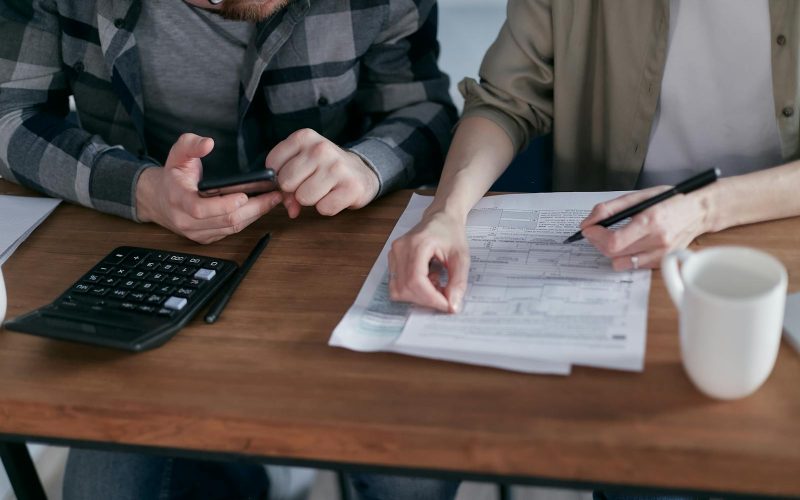 A couple diligently reviews their finances using a calculator and documents at home.